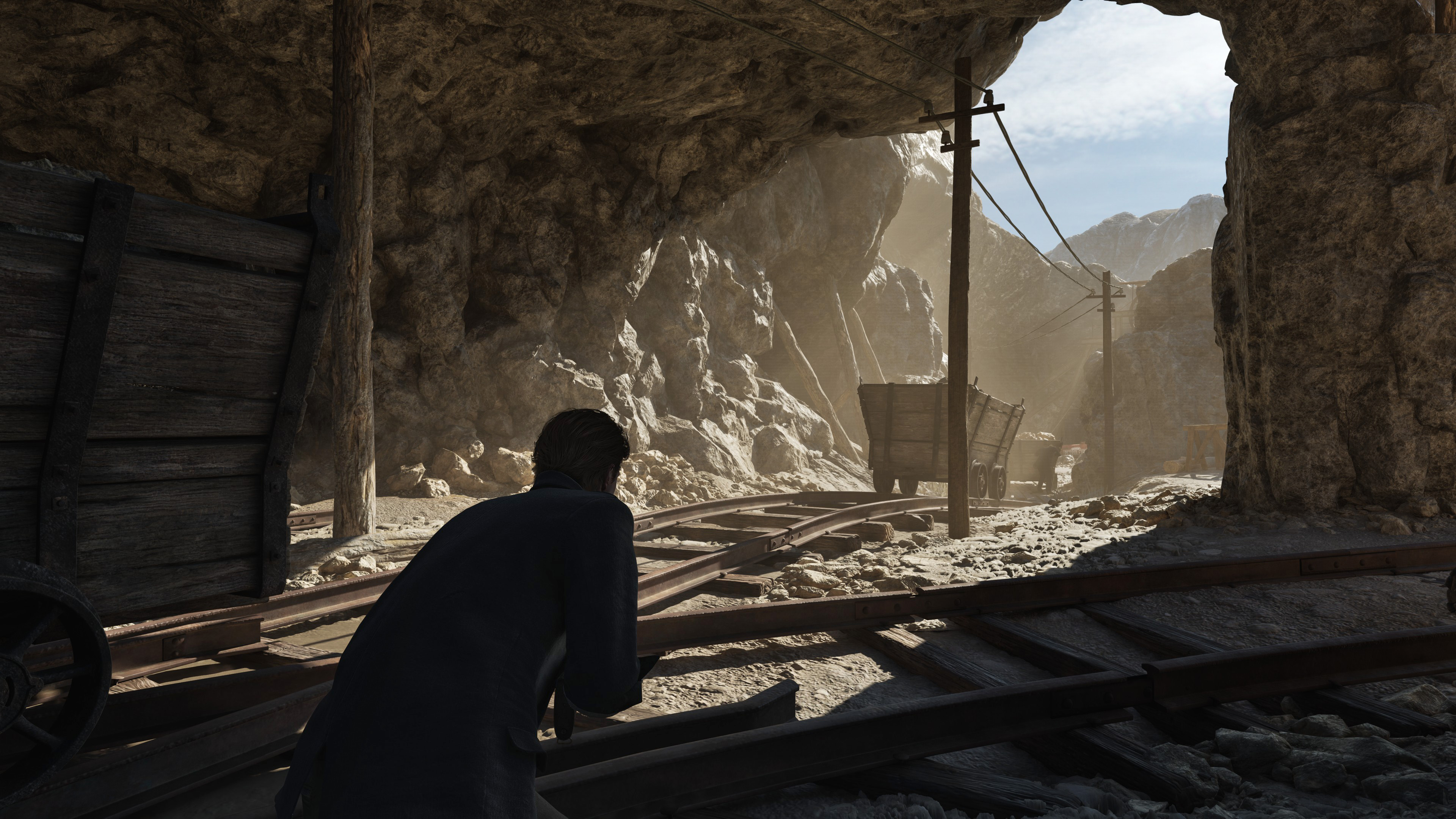 Mine tunnel mouth opening onto bright sunlit rock and ore carts